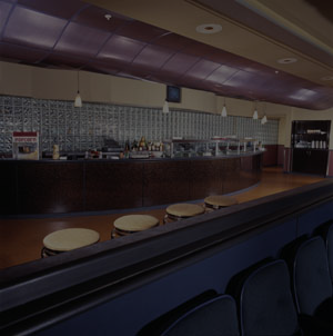 A retro style restaurant with the bar in the background and stools in the foreground