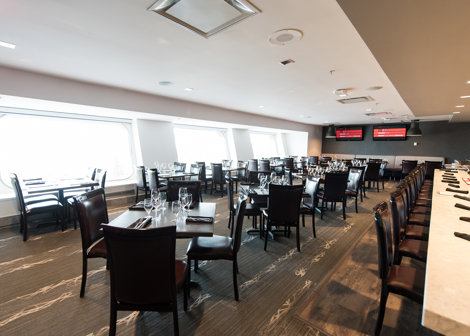 A restaurant with large windows has tables set with glasses, cutlery and napkins