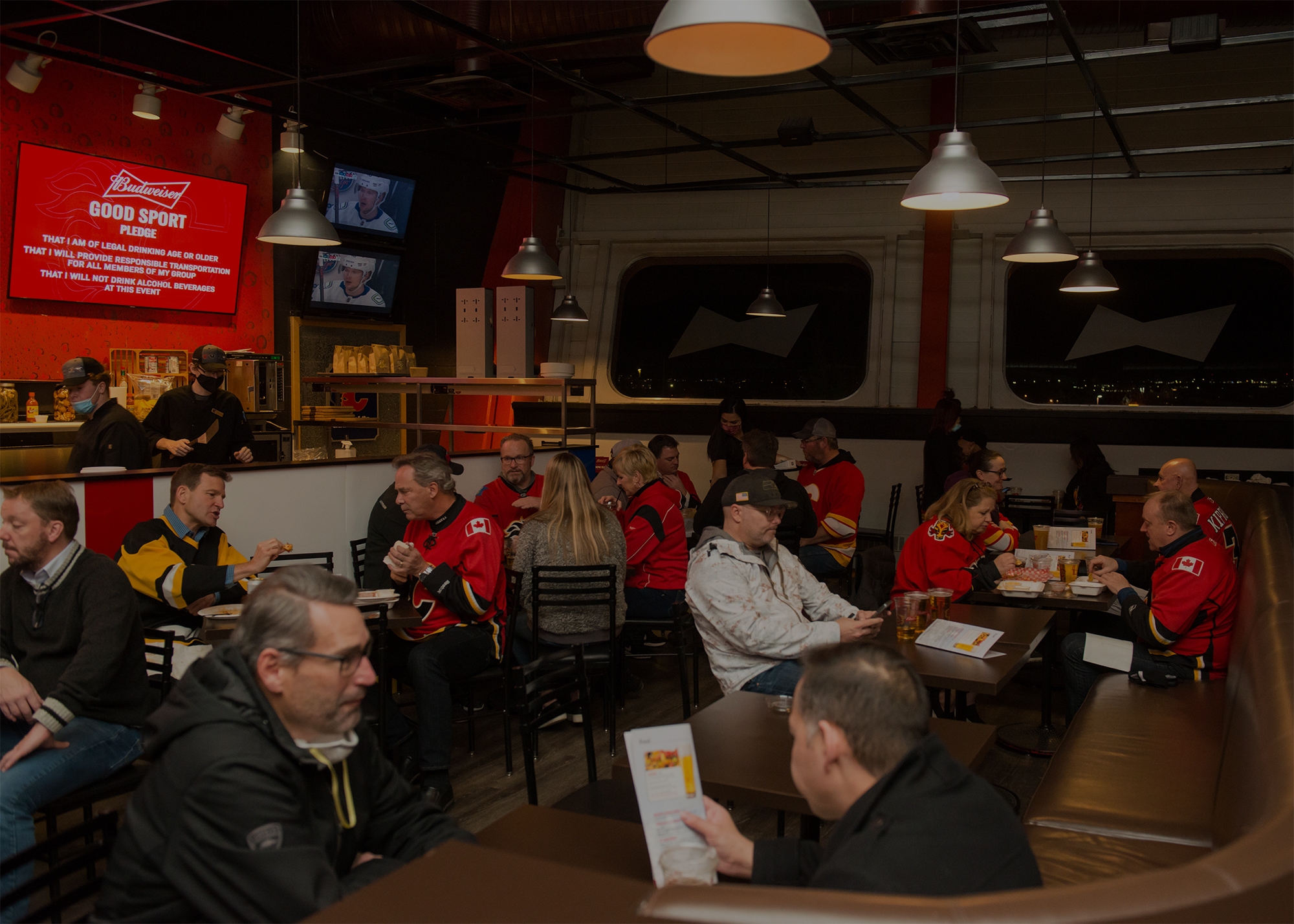 People wearing Calgary Flames jerseys sitting at tables ordering food and drinks inside the King Club