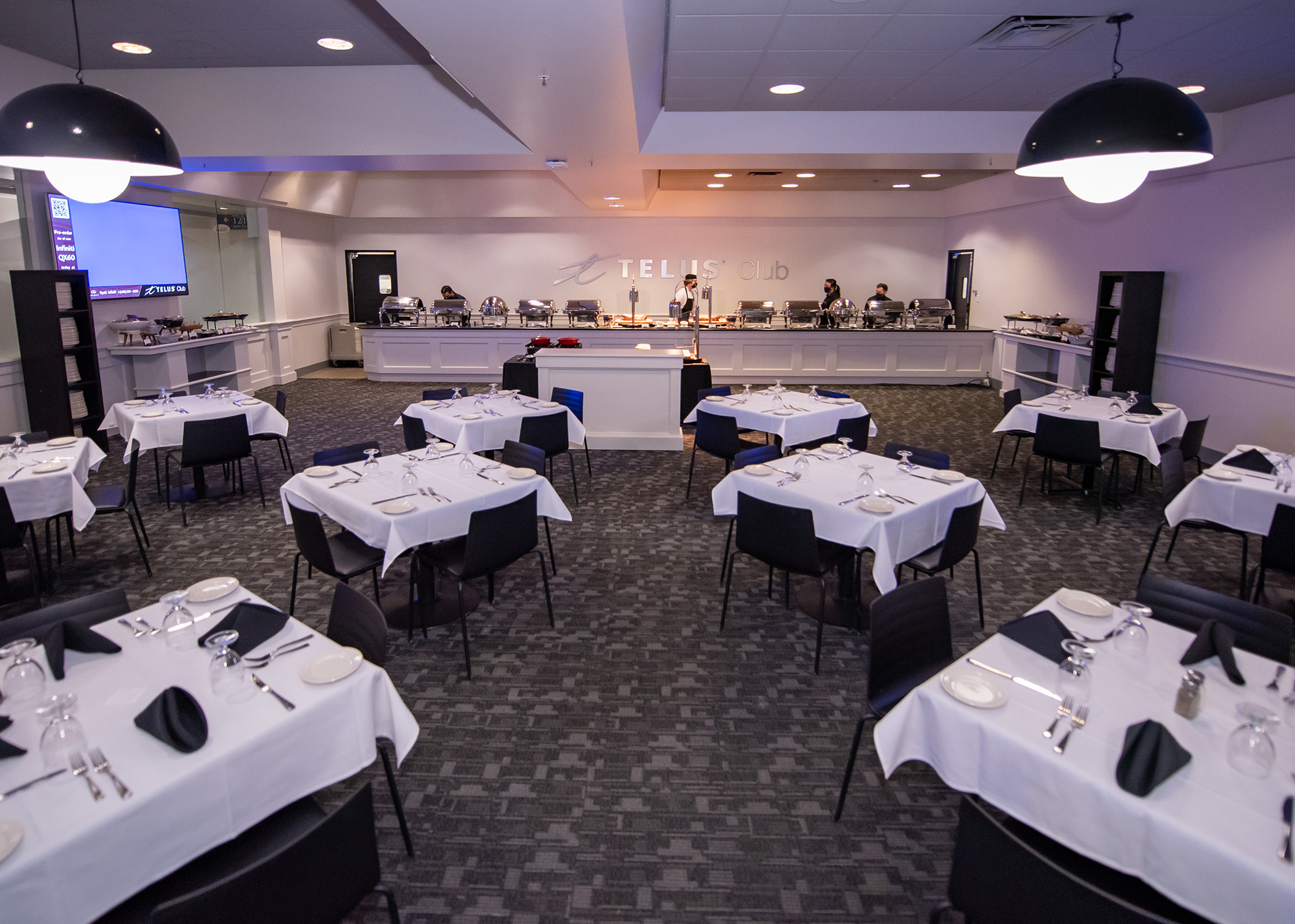 Inside the Telus Club, tables set with a white table cloth, black napkins, cutlery, plates and glasses